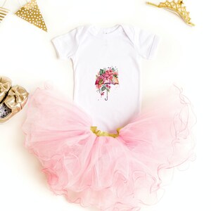 Może przedstawiać: Biały body dla niemowlęcia z nadrukiem r&oacute;żowego i zielonego parasola z kwiatami. Body jest zestawiony z r&oacute;żową tiulową sp&oacute;dniczką i złotymi butami.