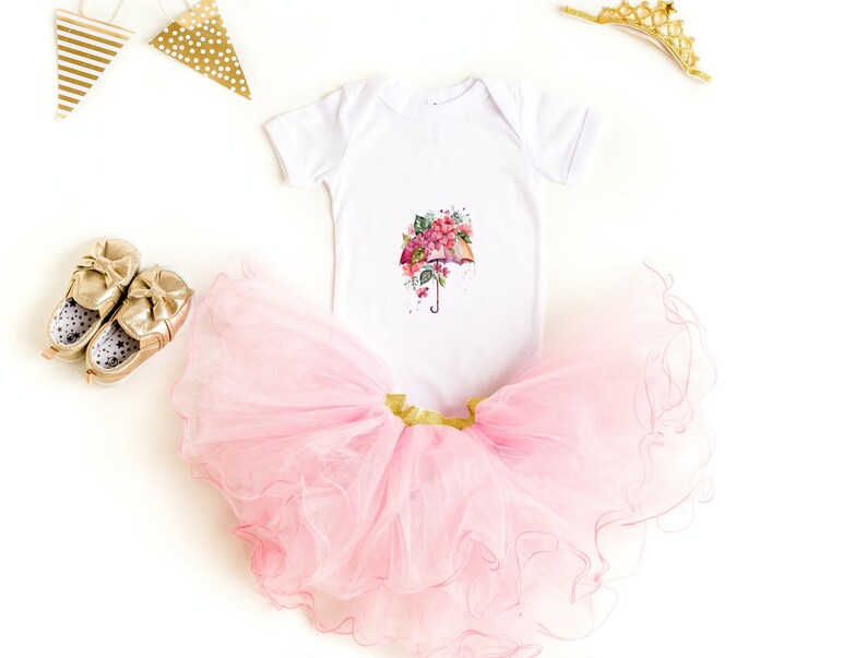 Może przedstawiać: Biały body dla niemowlęcia z nadrukiem r&oacute;żowego i zielonego parasola z kwiatami. Body jest zestawiony z r&oacute;żową tiulową sp&oacute;dniczką i złotymi butami.