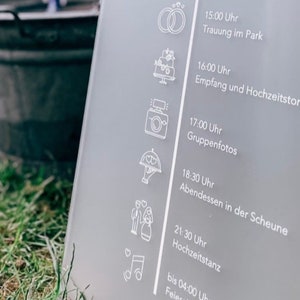 Könnte beinhalten: Ein weißes Acrylschild mit einem Hochzeitsplan für Sina & Stefan am 17. Juni 2023. Das Schild listet die Zeiten und Aktivitäten für den Hochzeitstag auf, darunter die Begrüßung, die Trauung, der Empfang, das Abendessen und das Tanzen.