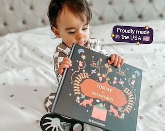 Può includere: Un libro con copertina rigida intitolato Tommy in Dreamland di Sue Donhym con una copertina scura che presenta illustrazioni di una casa, animali e motivi floreali. Un grafico viola riporta la scritta Proudly made in the USA con una bandiera.