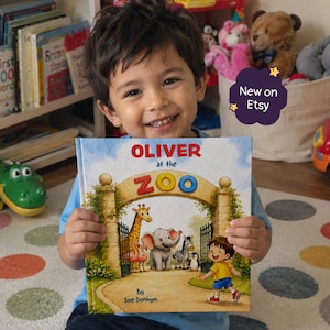May include: A hardback children's book titled Oliver at the Zoo by Sue Donhym. The cover features a colourful illustration of a boy walking towards a zoo entrance gate with a giraffe, elephant, zebra, penguin, and flamingos. The text New on Etsy is visible.