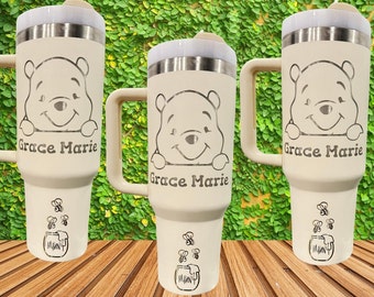 May include: Three white stainless steel tumblers with a Winnie the Pooh design. Each tumbler has a black handle and the name "Grace Marie" engraved on the front. The tumblers are decorated with a honey pot and bees.