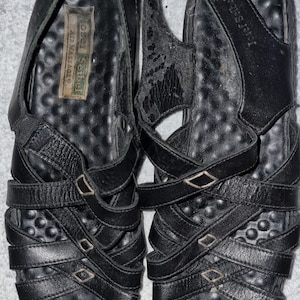 Puede incluir: Par de sandalias de cuero negro con múltiples correas y pequeñas hebillas metálicas. Las sandalias tienen una plantilla texturizada y un diseño de tiras traseras. La marca "Josef Seibel" es visible en la plantilla.