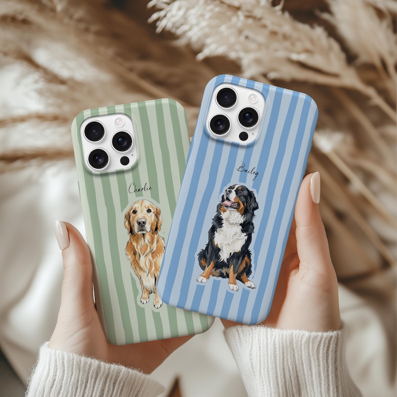Op de afbeelding: Twee telefoonhoesjes met hondenillustraties. E&eacute;n hoesje is lichtgroen met verticale strepen en een golden retriever-afbeelding, met het label "Charlie". De andere is lichtblauw met verticale strepen en een afbeelding van een Berner Sennenhond, met het label "Bailey".
