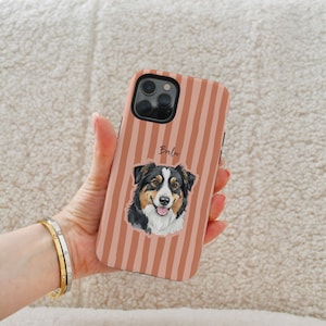 Op de afbeelding: Telefoonhoesje met verticale strepen in perzik- en bruintinten. Het heeft een illustratie van een hond met zwart, bruin en wit haar. De naam "Balu" staat boven de illustratie.