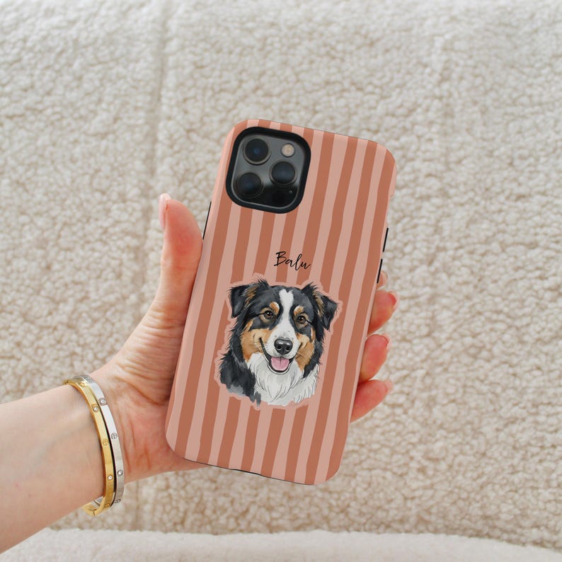 Op de afbeelding: Telefoonhoesje met verticale strepen in perzik- en bruintinten. Het heeft een illustratie van een hond met zwart, bruin en wit haar. De naam "Balu" staat boven de illustratie.