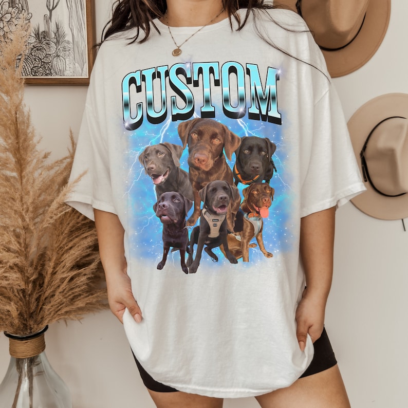 Pode incluir: Camiseta branca com a palavra "CUSTOM" impressa em letras azuis e brancas. A camiseta apresenta um gr&aacute;fico de seis labradores marrons com raios no fundo.