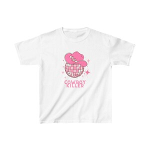 May include: White t-shirt featuring a pink disco ball wearing a pink cowboy hat with the text "COWBOY KILLER" underneath.