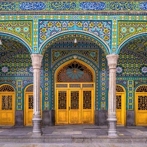 Pode incluir: Uma fachada arquitetônica ornamentada com entradas em arco. A estrutura apresenta intrincados mosaicos em tons de azul-petróleo, amarelo e azul. Portas douradas e colunas brancas realçam a grandiosidade do edifício. A parte superior da estrutura tem escrita árabe.