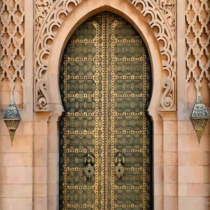 May include: An elaborate arched doorway featuring a large brass door with intricate detailing. The door is set within stone walls and decorative carvings. Two hanging lanterns enhance the architectural design. The image reflects a rich cultural heritage.