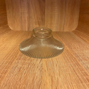 May include: A clear glass lampshade with a fluted design. The lampshade is round and has a wide base.