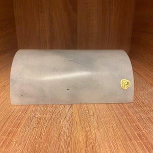 May include: A white, curved, rectangular box with a gold sticker that says "F.M.S." on it.