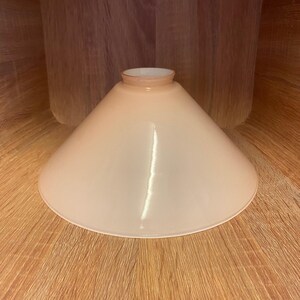 May include: A light pink glass lampshade with a wide, conical shape.