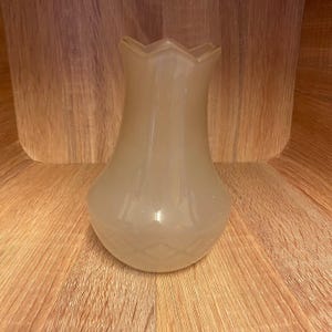May include: A white glass vase with a fluted rim and a slightly pear-shaped body. The vase has a subtle, textured pattern.