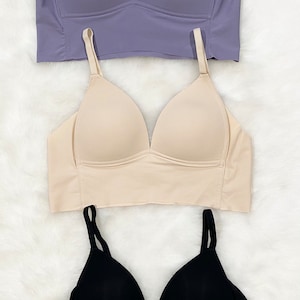 Könnte beinhalten: Drei nahtlose BHs in verschiedenen Farben: Lila, Beige und Schwarz. Jeder BH hat verstellbare Träger und einen tiefen Ausschnitt.