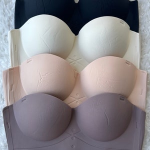 Puede incluir: Cuatro sujetadores sin tirantes en diferentes colores: negro, blanco, nude y gris. Los sujetadores están hechos de un material suave y elástico y tienen un diseño sin costuras.