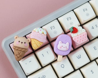 Könnte beinhalten: Fünf bunte Tastenkappen mit niedlichen Comic-Eis-, Cupcake- und Eis am Stiel-Designs. Die Tastenkappen befinden sich auf einer weißen Tastatur mit schwarzen Tasten.