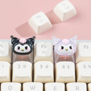 Puede incluir: Dos teclas de teclado negras y blancas con un dise&ntilde;o de personaje de dibujos animados. El personaje tiene una nariz rosa, ojos negros y una calavera en la cabeza. Las teclas est&aacute;n en un teclado blanco.