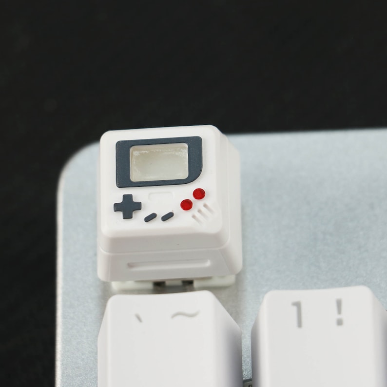 May include: White keyboard keycap with a black and gray Game Boy design. The keycap has a red and gray button design and a gray screen.