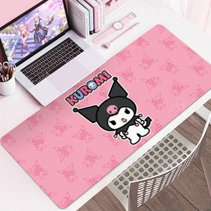 Puede incluir: Alfombrilla de escritorio rosa con el personaje Kuromi de Sanrio. La alfombrilla tiene un patr&oacute;n repetido de la cara de Kuromi y la palabra "KUROMI". Una computadora port&aacute;til, un reloj y bol&iacute;grafos est&aacute;n en el escritorio.