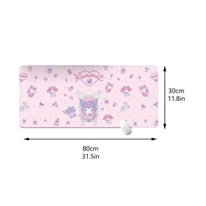 Puede incluir: Alfombrilla de escritorio rectangular rosa con dise&ntilde;o de dibujos animados. La alfombrilla presenta el texto "Kuromi" e ilustraciones de personajes de Kuromi, cupcakes y corazones. La alfombrilla mide 80 cm de largo y 30 cm de ancho.