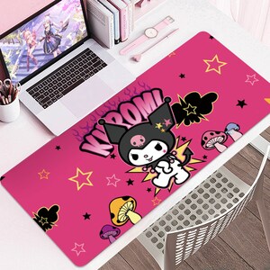 Puede incluir: Alfombrilla de escritorio rectangular rosa con un personaje de dibujos animados, estrellas y setas. La palabra &laquo;KROOM&raquo; est&aacute; escrita en una fuente estilizada. Tambi&eacute;n se ven un port&aacute;til, libros y un reloj rosa.
