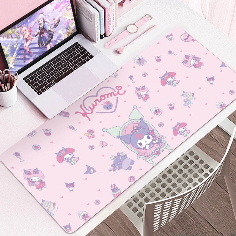 Puede incluir: Alfombrilla de escritorio rosa con un patr&oacute;n repetido de personajes de dibujos animados, cupcakes y corazones. La alfombrilla tiene la palabra "Kuromi" en un dise&ntilde;o en forma de coraz&oacute;n. Un port&aacute;til, un reloj y un bol&iacute;grafo est&aacute;n en el escritorio.