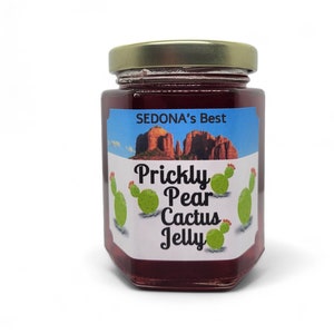 May include: A glass jar of prickly pear cactus jelly with a gold lid. The label is blue and white with the text "SEDONA'S Best" and "Prickly Pear Cactus Jelly". There are images of prickly pear cactus on the label.