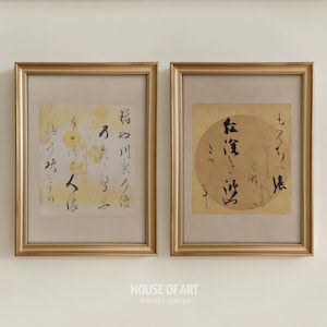 以下が含まれることがあります： 金色のフレームに入った2つのプリント。各プリントは、クリーム色の背景に日本の書道が施されています。1つは黄色の背景に円形のデザインがあります。もう1つは、ベージュの背景に円形のデザインがあります。