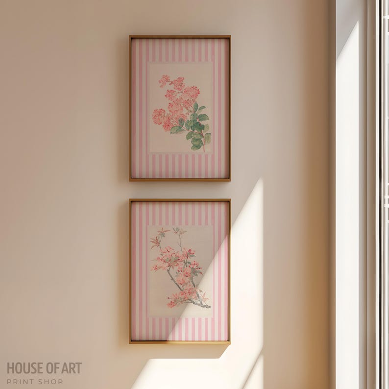 May include: Two framed floral prints. Each print features a botanical illustration of pink flowers and green leaves. The background has a pink and white striped pattern. The frames are a warm gold color. The text "HOUSE OF ART PRINT SHOP" is at the bottom.