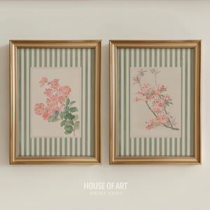 May include: Two framed floral prints. Each print features a gold frame, a green and white striped background, and a floral illustration. One print shows pink flowers with green leaves, and the other shows pink flowers on a branch.
