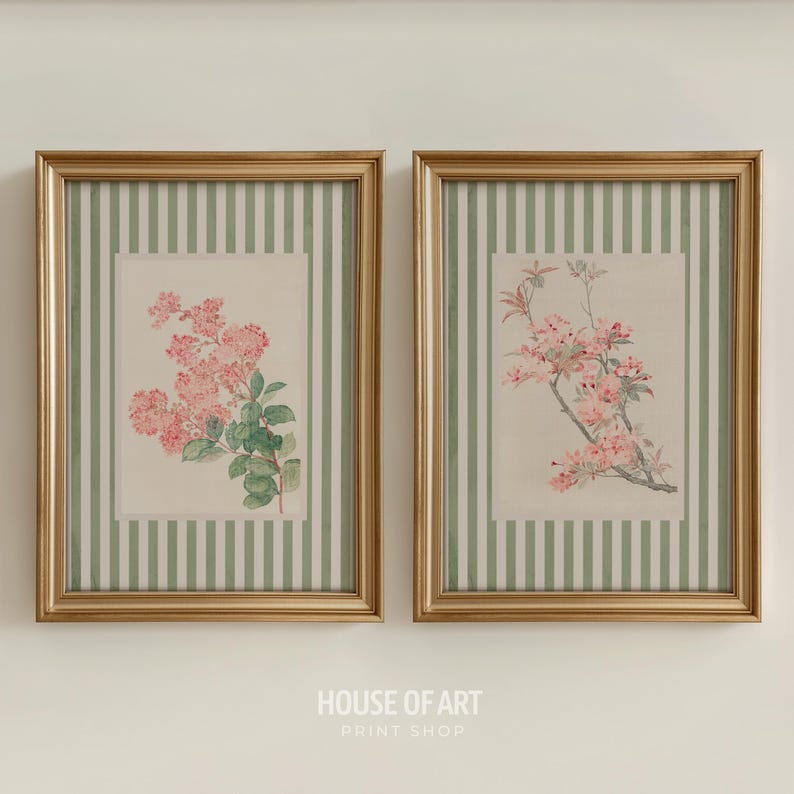 May include: Two framed floral prints. Each print features a gold frame, a green and white striped background, and a floral illustration. One print shows pink flowers with green leaves, and the other shows pink flowers on a branch.