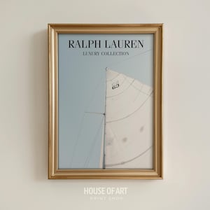May include: A framed print featuring a sailboat with a white sail against a light blue sky. The print is in a gold-colored frame. The text "RALPH LAUREN LUXURY COLLECTION" is at the top. The text "HOUSE OF ART PRINT SHOP" is at the bottom.