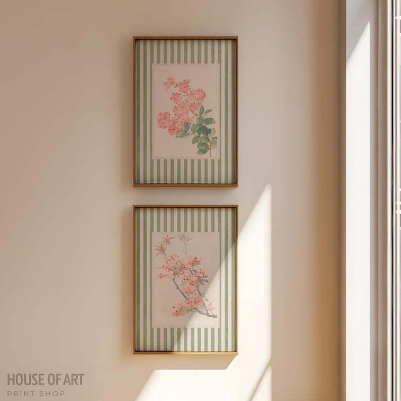 May include: Two framed floral prints. Each print features a pink floral arrangement on a cream background with a green striped border. The frames are a warm brown color. The prints are hanging on a cream-colored wall.