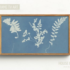 May include: A framed print of a blue cyanotype featuring white silhouettes of ferns. The print is in a natural wood frame.