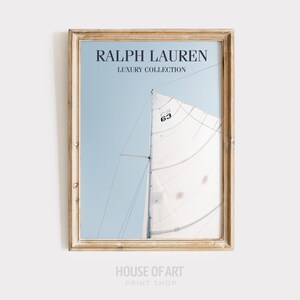 May include: Framed print featuring a sailboat with a white sail against a light blue sky. The print includes the text "RALPH LAUREN LUXURY COLLECTION" at the top. The frame is a light, distressed wood. The number "63" is visible on the sail.