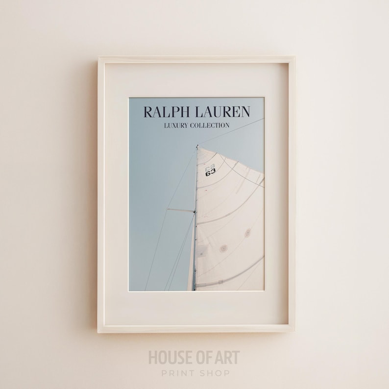 May include: Framed print featuring a sailboat with a white sail against a light blue sky. The print includes the text "RALPH LAUREN LUXURY COLLECTION" at the top. The frame is white, and the print is from the "HOUSE OF ART PRINT SHOP".