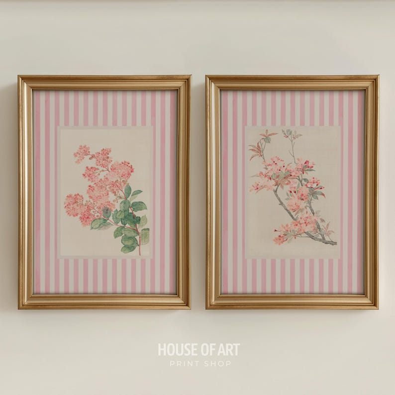 May include: Two framed floral prints. Each print features a botanical illustration of pink flowers and green leaves. The frames are gold, and the background of each print has a pink and white striped pattern. The text "HOUSE OF ART PRINT SHOP" is at the bottom.