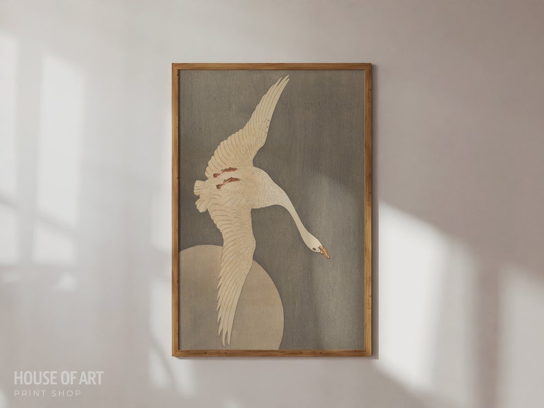 Op de afbeelding: Een ingelijste print van een witte vogel met bruine markeringen die vliegt tegen een grijze achtergrond. De vogel is in klassieke Japanse stijl.