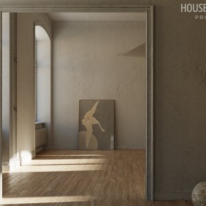 Op de afbeelding: Een minimalistisch interieurontwerp met een grote, ingelijste abstracte kunstprint op een lichtgrijze muur. De kamer heeft een houten vloer en een groot raam met natuurlijk licht dat naar binnen stroomt.