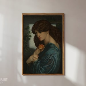 May include: A painting of a woman with long, dark hair, wearing a blue dress and holding a red fruit. The painting is framed in a wooden frame.
