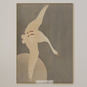 Op de afbeelding: Een witte vogel met uitgespreide vleugels vliegt tegen een grijze achtergrond. De vleugels van de vogel zijn wijd uitgespreid en zijn kop is naar beneden gekanteld. De achtergrond is een gedempt grijs, met een vleugje bruin. De vogel is scherp in focus, terwijl de achtergrond licht wazig is. De afbeelding is een traditionele Japanse houtsnede.