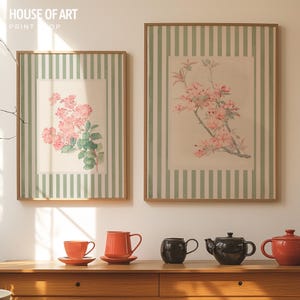 May include: Two framed floral prints with pink flowers and green leaves, set against a striped background. The prints are displayed above a wooden table with orange teacups, saucers, and teapots. The text "HOUSE OF ART PRINT SHOP" is visible.