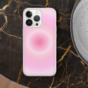 May include: A white iPhone case with a pink and white gradient design. The case has a circular pattern in the center and a camera lens cutout.