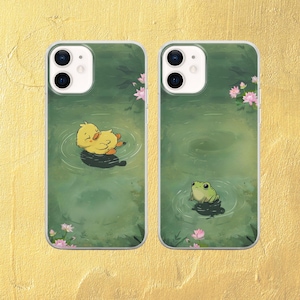 May include: Two phone cases with a green background and a pond scene. One case features a yellow duckling floating on the water and the other case features a green frog sitting on a lily pad.
