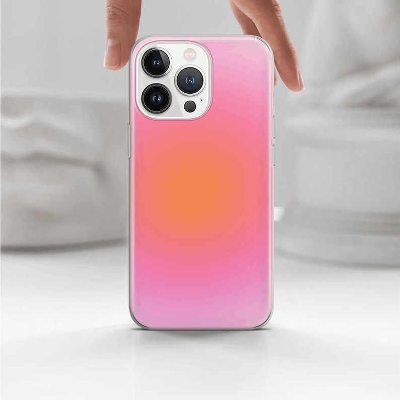 May include: A clear phone case with a pink to orange gradient. The case has a raised camera bump with three lenses.