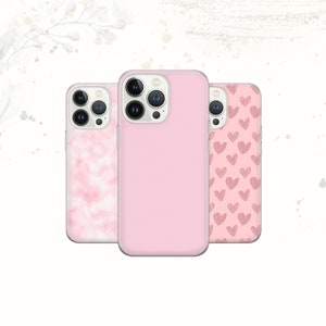 Könnte beinhalten: Drei rosa Handyhüllen. Die mittlere Hülle ist einfarbig rosa, während die anderen beiden Muster aufweisen: eine mit Aquarelleffekt und die andere mit einem Herzdesign. Die Hüllen sind für ein Smartphone konzipiert.