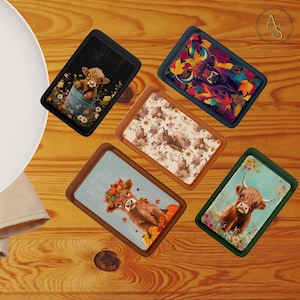 May include: Five rectangular trays with Highland cow illustrations. The trays display images of cows in different settings, such as a bucket, autumn leaves, and floral patterns. The trays have brown wooden frames and are arranged on a wooden surface.