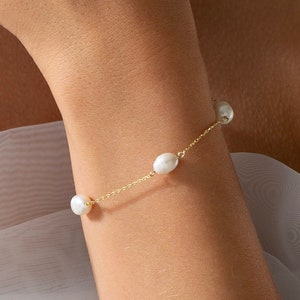 May include: A delicate gold chain bracelet with four white pearls. The bracelet is on a person's wrist.