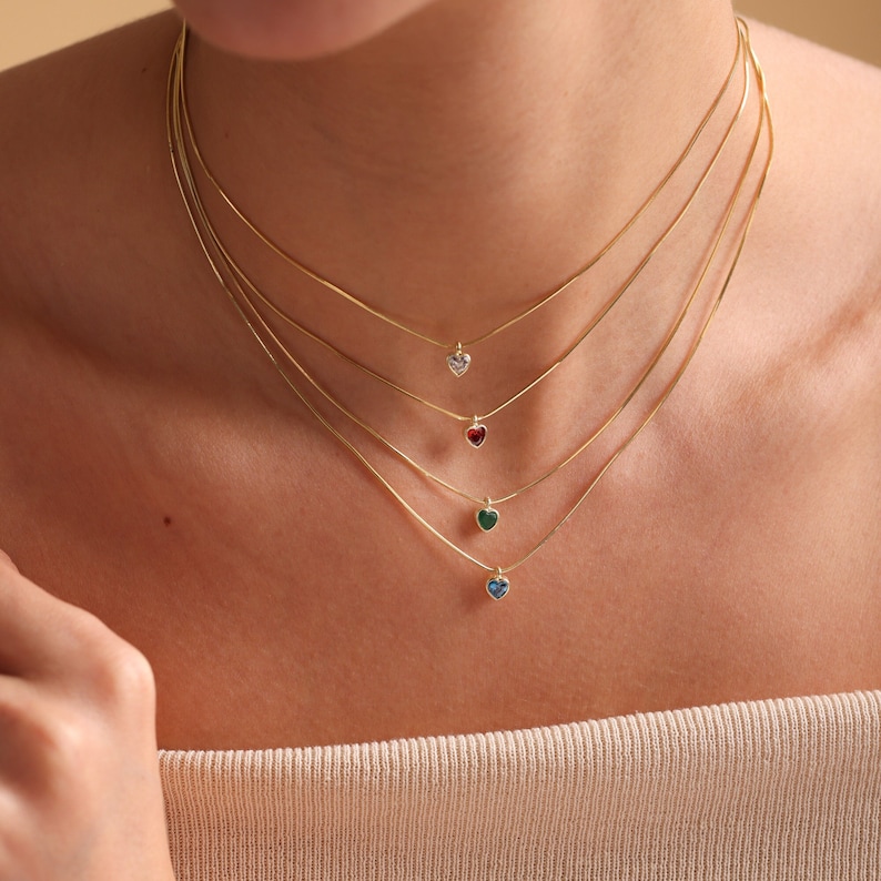 Puede incluir: Un collar de cadena de oro en capas con cuatro colgantes en forma de coraz&oacute;n. Los colgantes est&aacute;n adornados con piedras preciosas transparentes, rojas, verdes y azules.